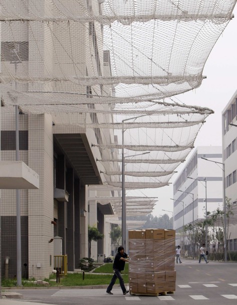 A worker pushes a trolley carrying products under nets which are installed on a factory building to prevent workers from jumping to their deaths at a Foxconn factory in Langfang